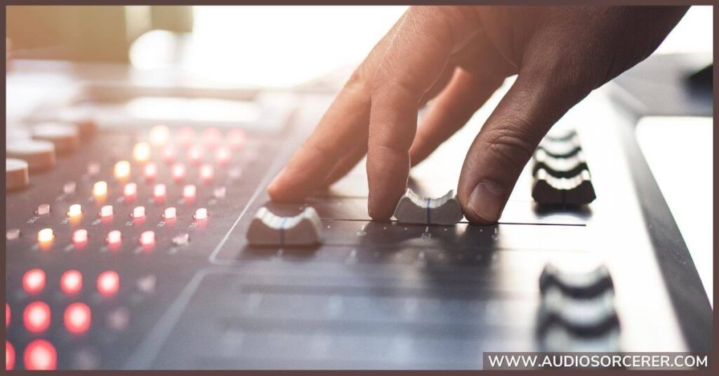 A closeup of a hand on a mixing board moving faders.