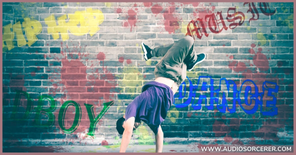 A guy dancing with a brick wall behind him with graffiti on it that says Hip Hop.