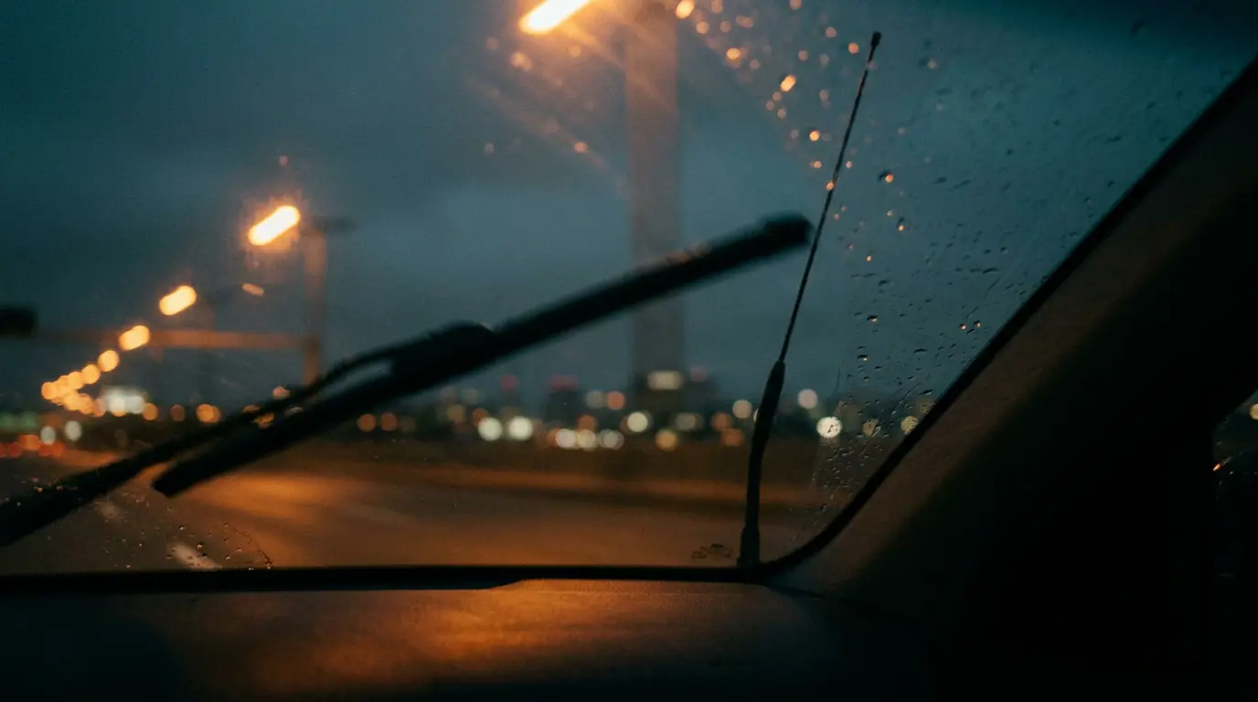 Nighttime view from a moving car, antenna against windshield, amber streetlight trails blurring into blue dusk