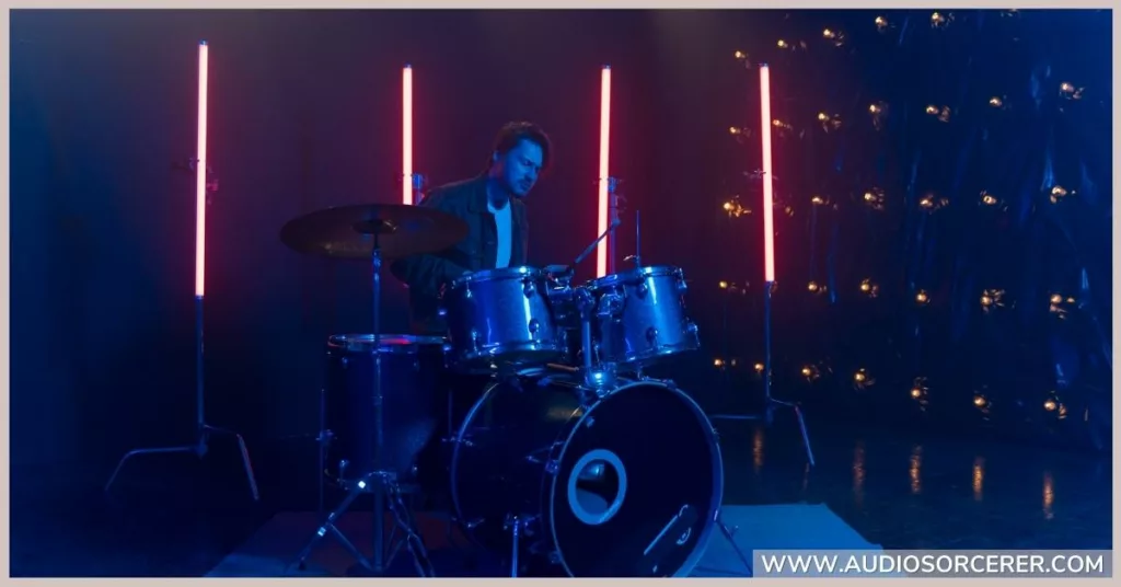 Man playing a drum kit with neon lights in the background.