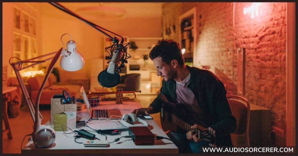 A man sitting at a desk with a guitar in his hand writing a song.