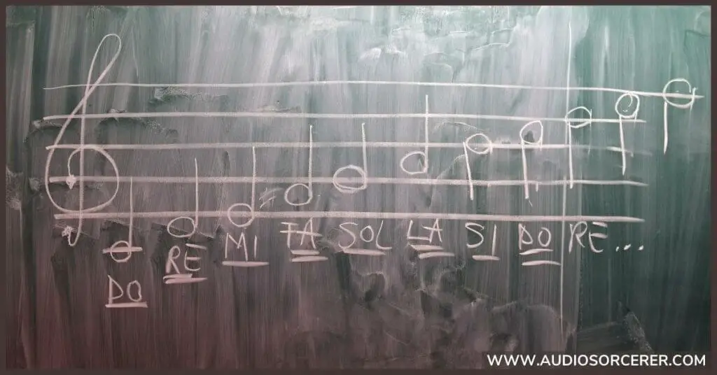 Solfege notes on a treble clef staff written on a chalk board.
