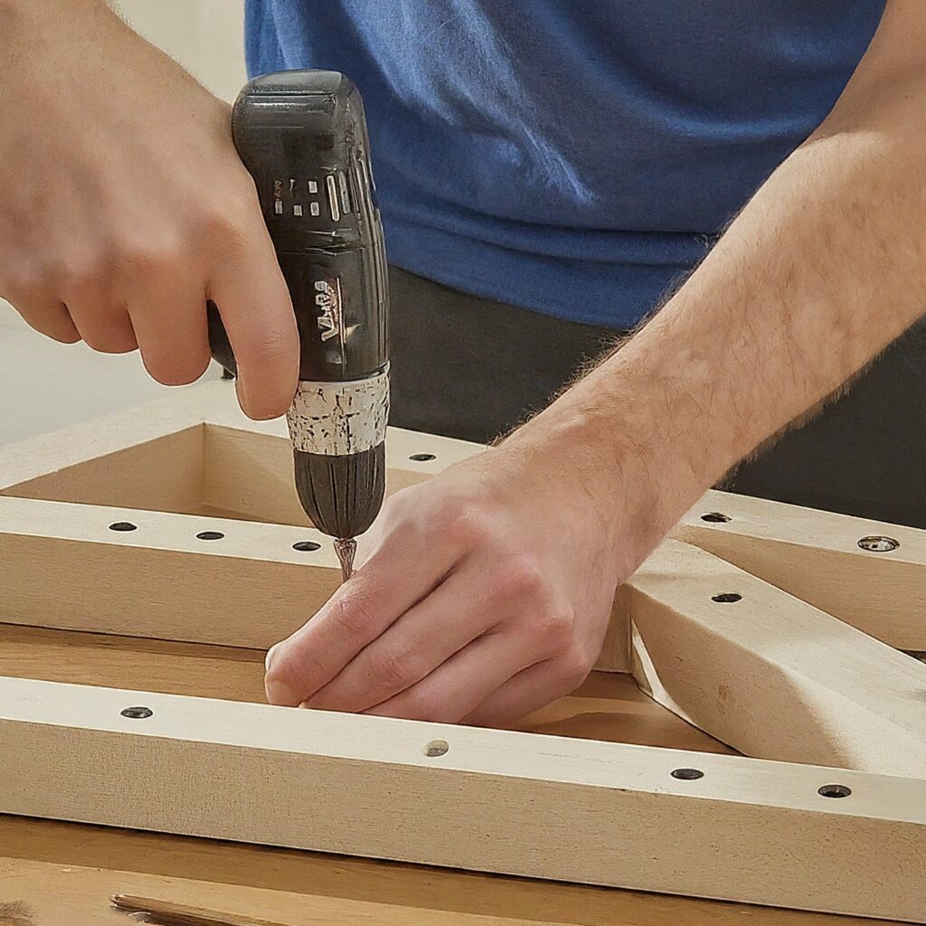 Man drilling screws into a frame for a diy bass trap.
